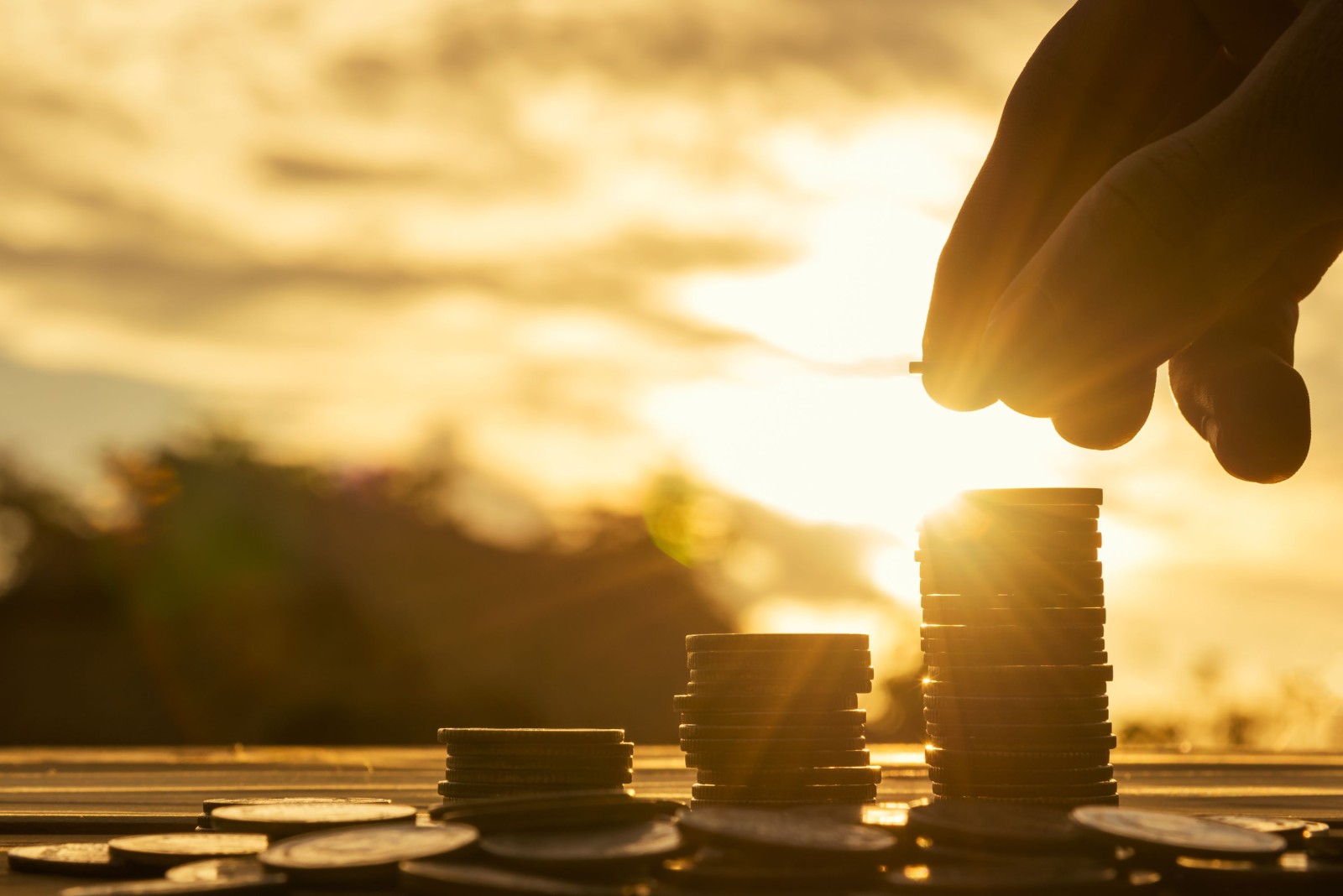 Koncepcja oszczędzania pieniędzy ustawiona przez męską rękę wkładającą stos monet do rosnącego biznesu. Close up of hand on sunset background, money concept, Business Finance and Money concept, Save money for prepare in the future. money silhouette.