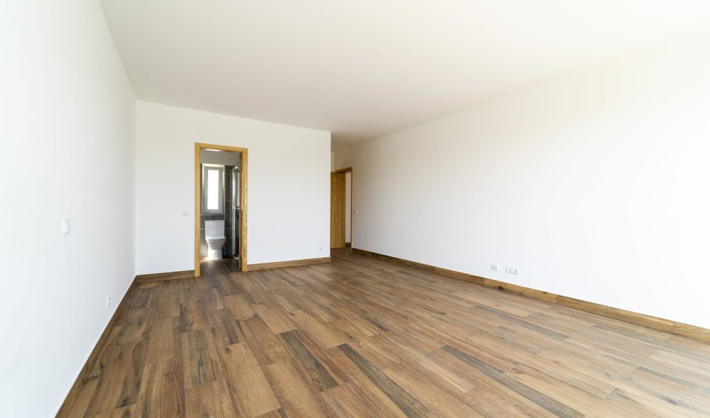 Pusty pokój z ciemną drewnianą podłogą laminowaną. Wnętrze domu, szeroka sypialnia lub pokój dzienny. Niedawno pomalowane nowe mieszkanie lub dom. Drewniana podłoga. Zarządzanie nieruchomościami