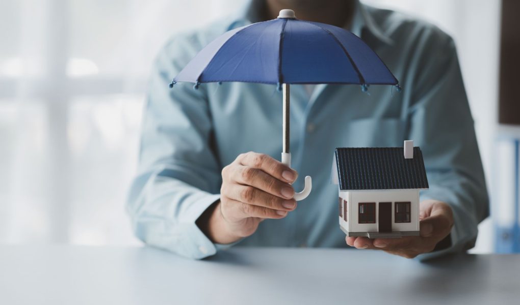 Osoby posiadające małe parasole i modele domów, ubezpieczenia mieszkań od zbliżających się strat i pożaru, ubezpieczenia budynków od pożaru, koncepcje ubezpieczeń domów i nieruchomości.
