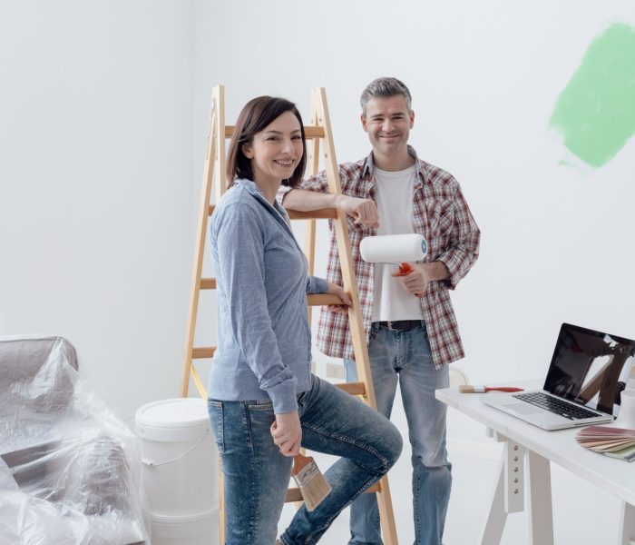 Uśmiechnięta para maluje swój dom, pozują i opierają się na drabinie koncepcja renowacji domu