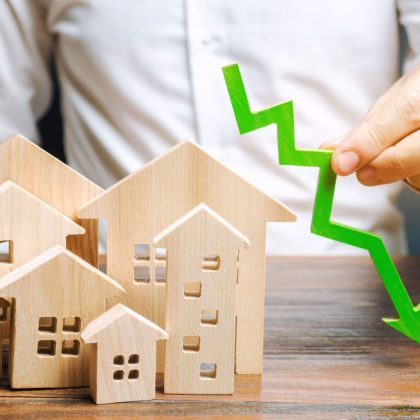 Analityk trzyma strzałkę w dół w pobliżu drewnianych domów. Koncepcja spadającego rynku nieruchomości. Niskie ceny i koszty mieszkań. Obniżone oprocentowanie kredytów hipotecznych i popyt na mieszkania. Upadłość. Kryzys i niska płynność