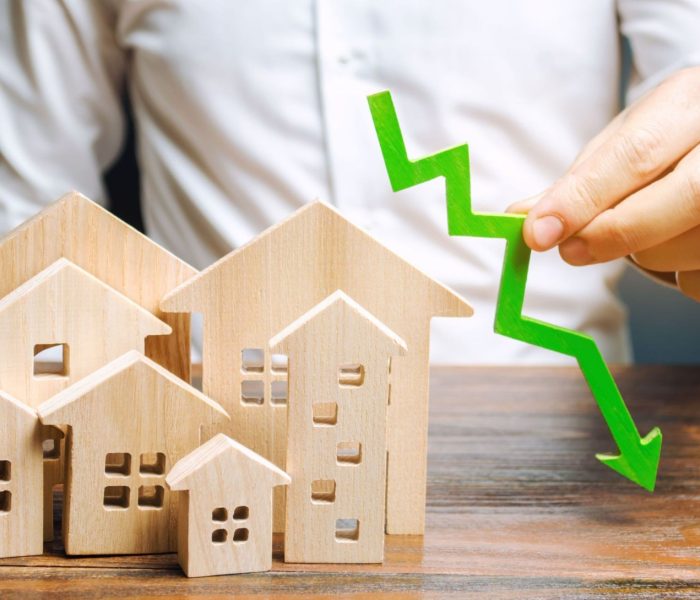 Analityk trzyma strzałkę w dół w pobliżu drewnianych domów. Koncepcja spadającego rynku nieruchomości. Niskie ceny i koszty mieszkań. Obniżone oprocentowanie kredytów hipotecznych i popyt na mieszkania. Upadłość. Kryzys i niska płynność