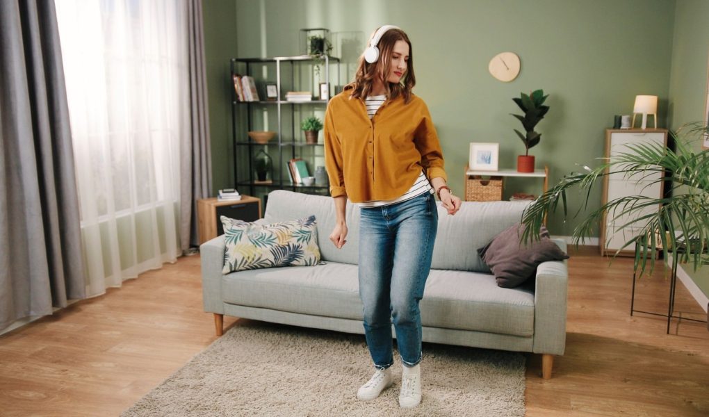 Kaukaska młoda piękna radosna kobieta tańczy w nowoczesnym salonie w domu samotnie słuchając muzyki w białych słuchawkach wykonując ruchy i dobrze się bawiąc. Koncepcja rytmu, tancerz domowy