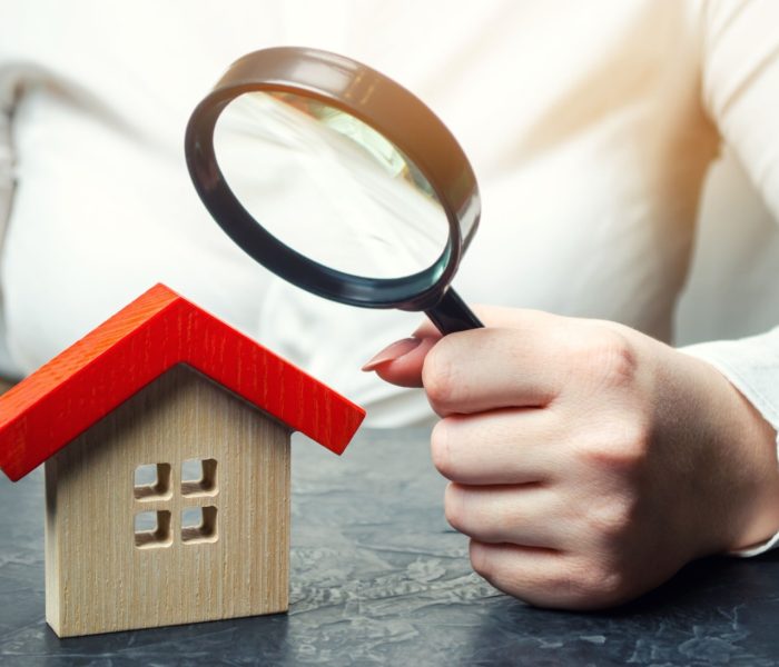 Kobieta trzyma szkło powiększające nad drewnianym domem. Rzeczoznawca nieruchomości. Ocena stanu domu. Wycena nieruchomości. Wyszukiwanie mieszkań i apartamentów.