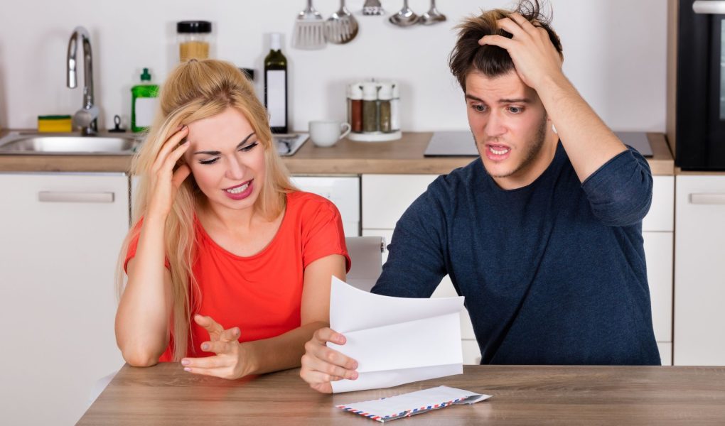 Młoda zmartwiona para czytająca list i rachunek w kuchni w domu. Koncepcja złych wiadomości