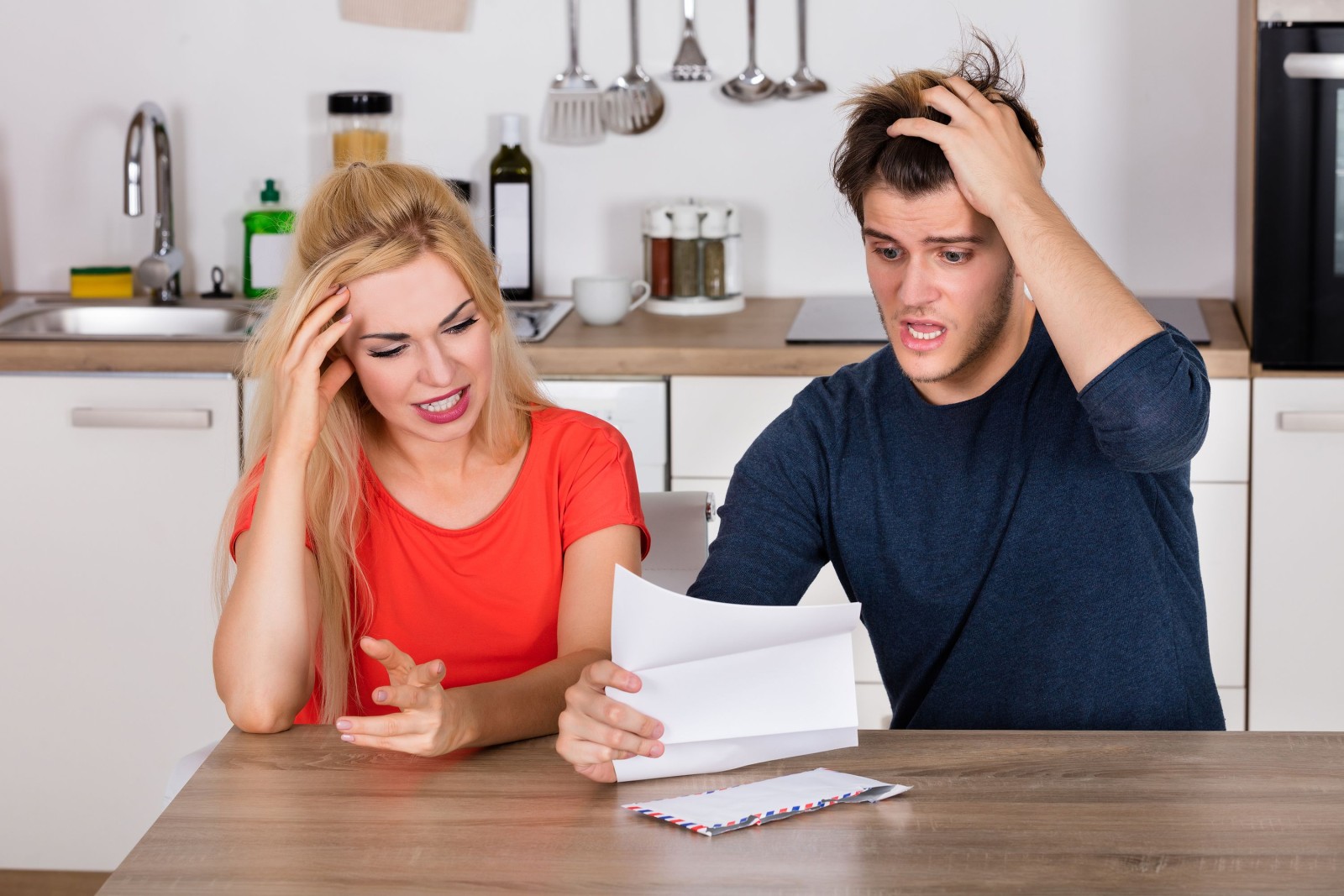 Młoda zmartwiona para czytająca list i rachunek w kuchni w domu. Koncepcja złych wiadomości