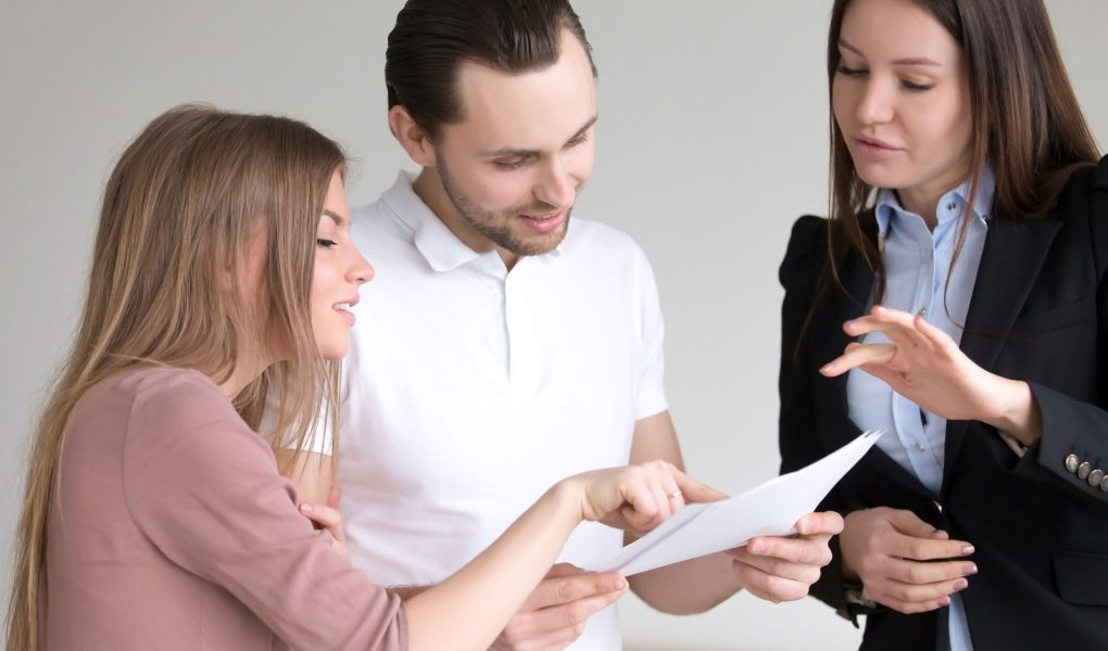 Klient płci męskiej trzymający dokumenty i uważnie je studiujący, omawiający ofertę z menadżerką i żoną, warunki umowy, rozważający kredyt bankowy, osobiste ubezpieczenie zdrowotne