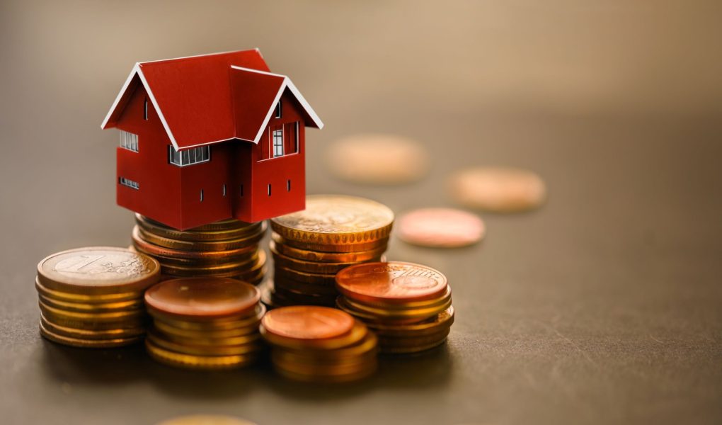 Miniaturowy dom na stosie monet. Pojęcie inwestycji w nieruchomości, pożyczek na nieruchomości, kredytów hipotecznych, podatków