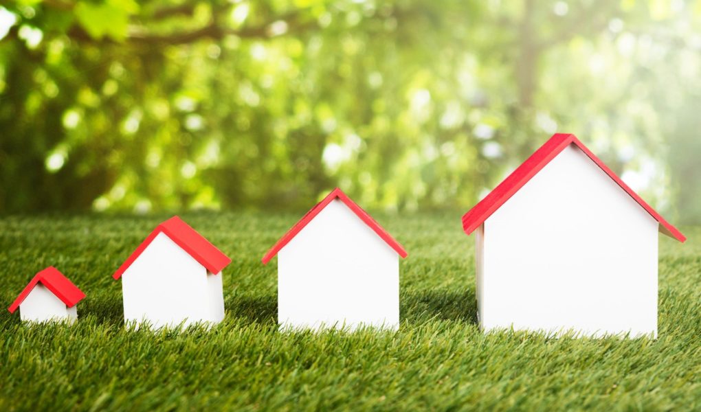 Różne rozmiary domów ułożonych w rzędzie na trawiastym polu