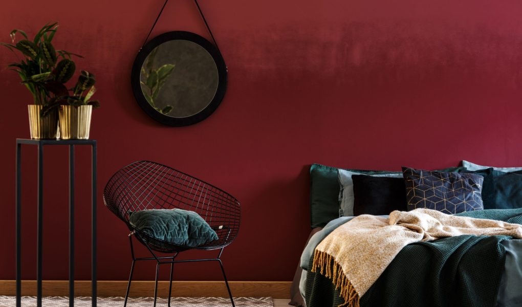 Granatowy drewniany fotel obok półek na tle czerwonej ściany z lustrem w eleganckim wnętrzu salonu