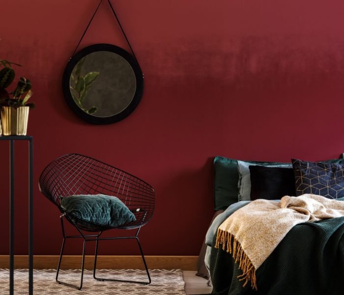 Granatowy drewniany fotel obok półek na tle czerwonej ściany z lustrem w eleganckim wnętrzu salonu