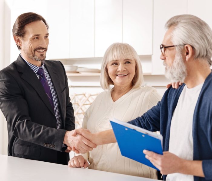 Spotkanie z przyszłymi właścicielami domu. Zachwycony, doświadczony, pozytywny agent nieruchomości spotykający się ze starą parą klientów podczas uścisku dłoni i prezentacji umowy