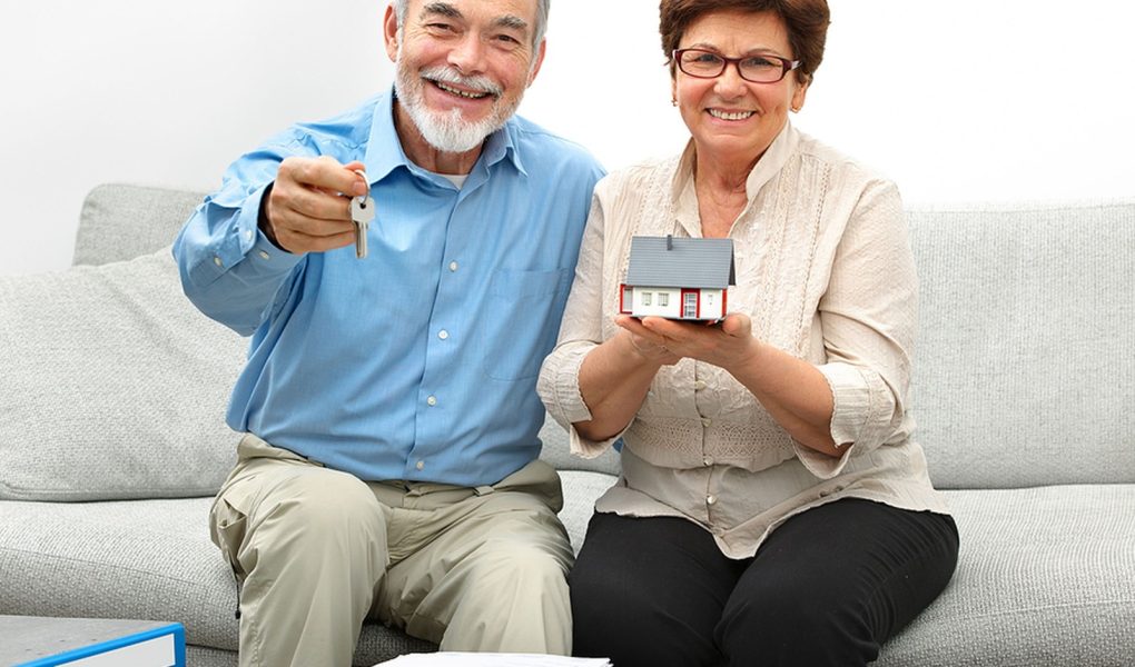 Szczęśliwa para seniorów trzymająca mały domek i klucze w rękach