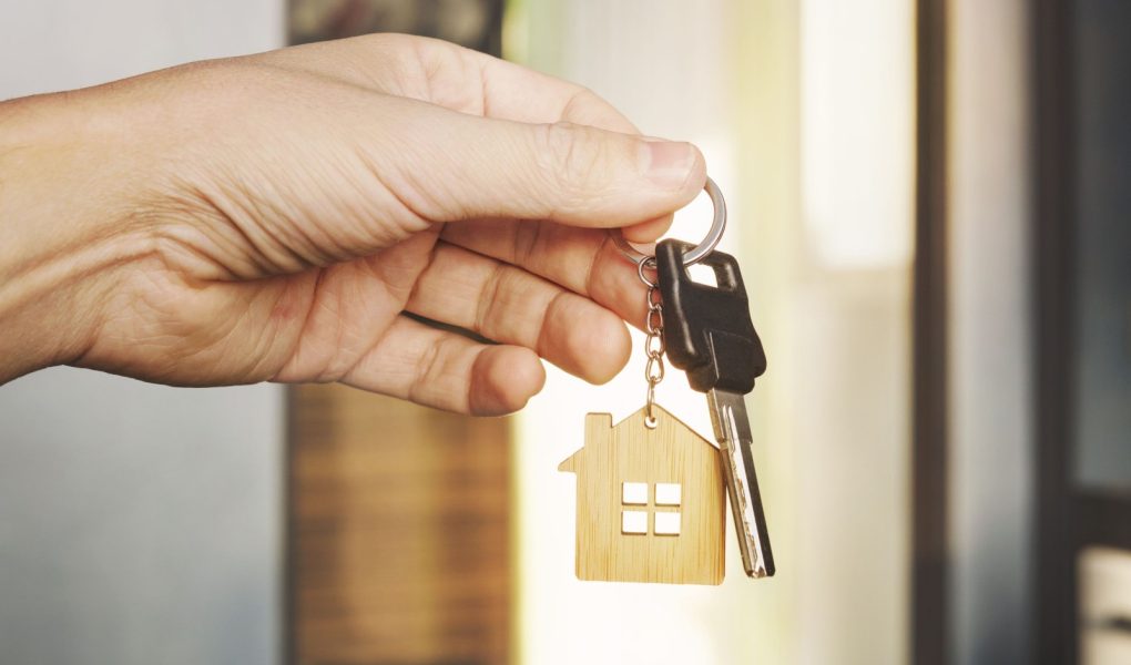 Klucz do domu w męskiej dłoni na tle mieszkania. brelok do kluczy. Koncepcja przeprowadzki do nowego mieszkania. Symbol zakupu domu. Inwestycja w nieruchomości. Kup nieruchomość. transakcja na rynku nieruchomości