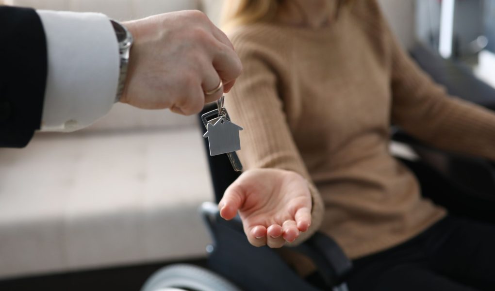 Zbliżenie na biznesmena wręczającego klucze od nowego domu niepełnosprawnej kobiecie. Kobieta siedząca na wózku inwalidzkim. Dzień przeprowadzki do mieszkania. Niepełnosprawni i koncepcja nieruchomości