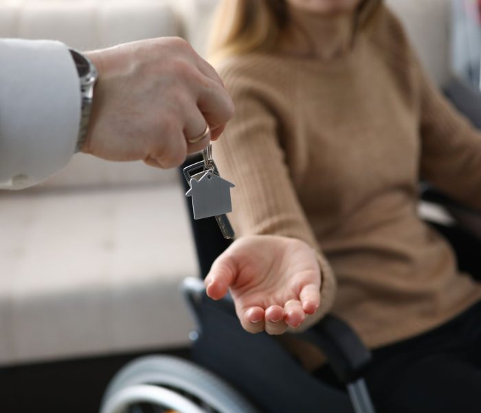 Zbliżenie na biznesmena wręczającego klucze od nowego domu niepełnosprawnej kobiecie. Kobieta siedząca na wózku inwalidzkim. Dzień przeprowadzki do mieszkania. Niepełnosprawni i koncepcja nieruchomości