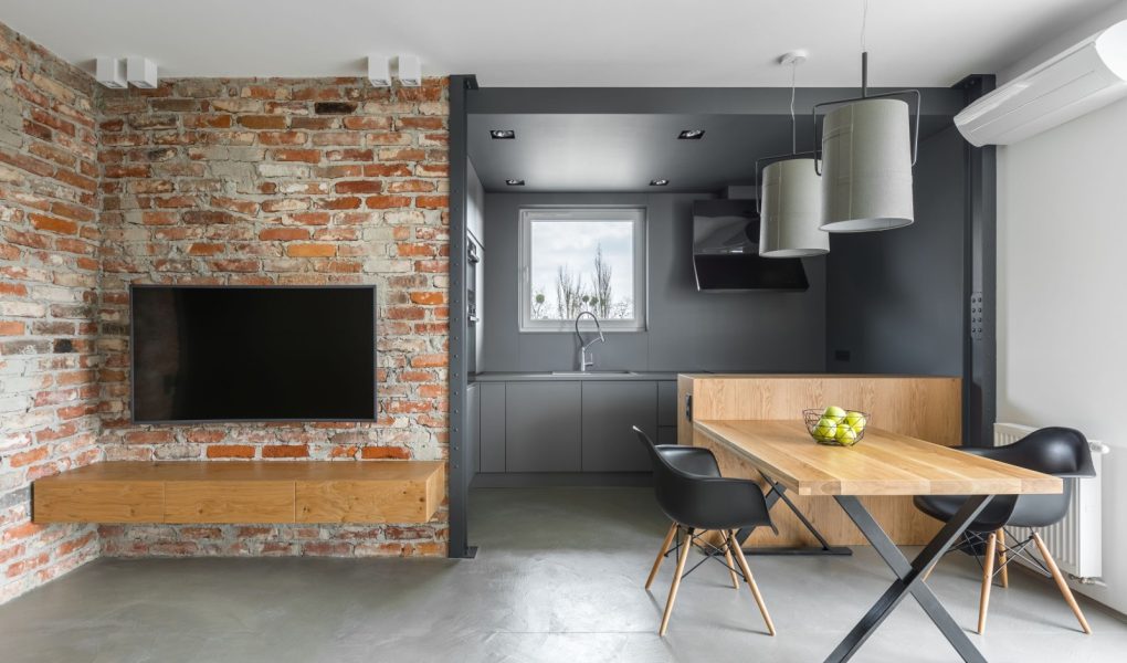 Wnętrze domu w stylu industrialnym z aneksem kuchennym, stołem telewizyjnym, krzesłami i ceglaną ścianą