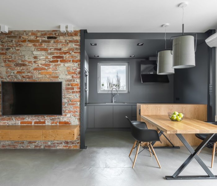 Wnętrze domu w stylu industrialnym z aneksem kuchennym, stołem telewizyjnym, krzesłami i ceglaną ścianą