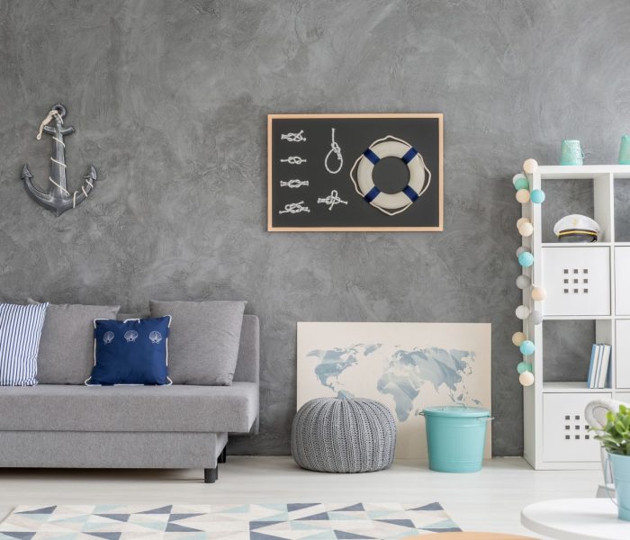 Szare wnętrze domu z marynistyczną dekoracją ścienną, sofą, dywanem i białym schowkiem