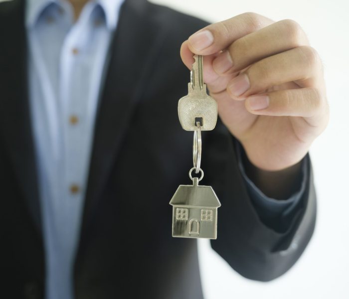 Koncepcja biznesmena z branży nieruchomości daje klucze do domu nowemu właścicielowi. Pośrednik trzyma w ręku brelok do kluczy.