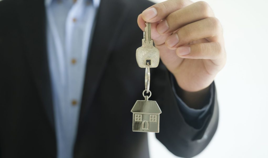 Koncepcja biznesmena z branży nieruchomości daje klucze do domu nowemu właścicielowi. Pośrednik trzyma w ręku brelok do kluczy.