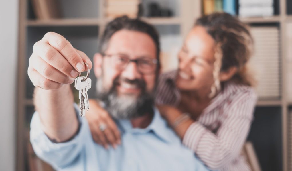 Nacisk na klucze, trzymane przez podekscytowanych młodych małżonków właścicieli domów. Szczęśliwa para małżeńska świętująca przeprowadzkę do nowego domu, demonstrująca klucze, stojąca w mieszkaniu, koncepcja kredytu hipotecznego na nieruchomości.