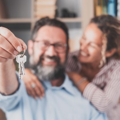 Nacisk na klucze, trzymane przez podekscytowanych młodych małżonków właścicieli domów. Szczęśliwa para małżeńska świętująca przeprowadzkę do nowego domu, demonstrująca klucze, stojąca w mieszkaniu, koncepcja kredytu hipotecznego na nieruchomości.