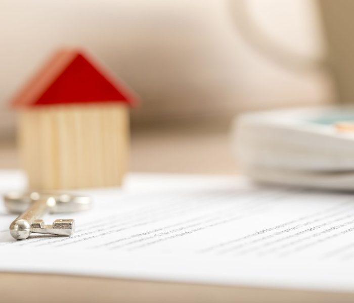 Zbliżenie umowy sprzedaży domu gotowej do podpisania z drewnianym zabawkowym kluczem do domu i kalkulatorem. Koncepcja kredytu hipotecznego i dzierżawy nieruchomości.